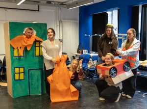 Fachschüler*innen Daemen, Marija, Mercedes, Noe, Lea und Alice beim Standbild "Es brennt!", das sie unter Anleitung von Suzanne Austin mit einfachen Materialien und Requisiten als Bühnenbild gestaltet haben.